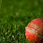 A close-up of a red cricket ball on grassy ground